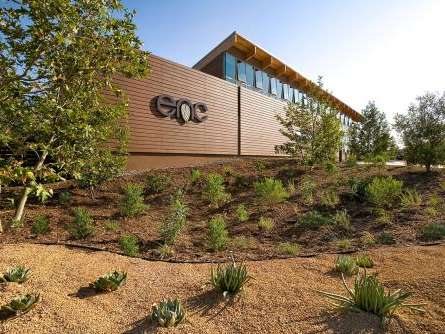 A building with "enc" written on the side. Landscaping with sparse desertous plants is in front. The sun shines. A building with "enc" written on the side. Landscaping with sparse desertous plants is in front. The sun shines.