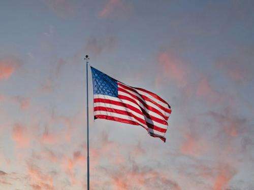An American flag waves against a background of a sunset. Whispy pink clouds stand out against a darkening blue sky. An American flag waves against a background of a sunset. Whispy pink clouds stand out against a darkening blue sky.